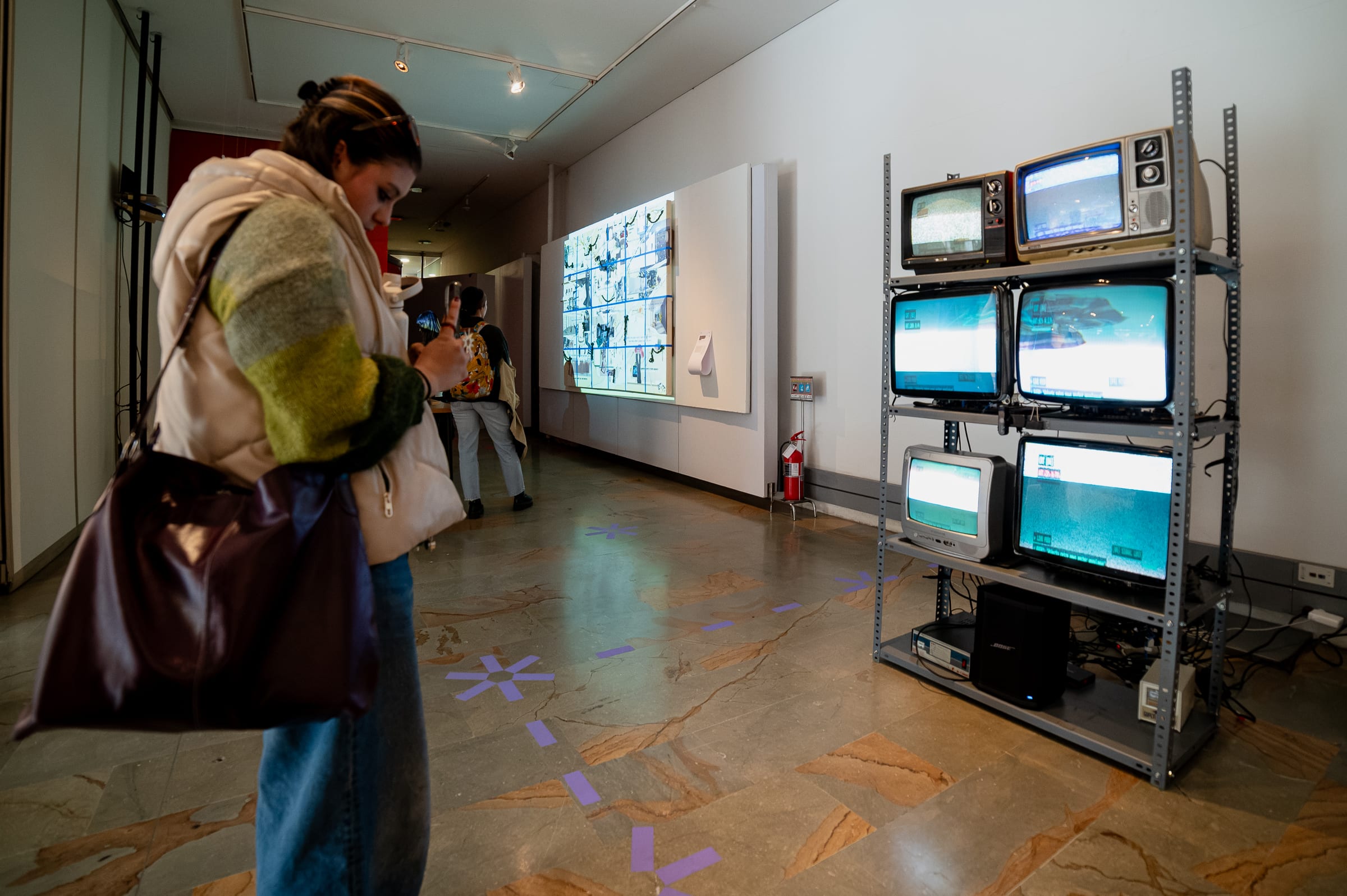 Gallery visitor looking down at her smartphone while standing on the purple antenna floor markers in front of the glowing CRT array