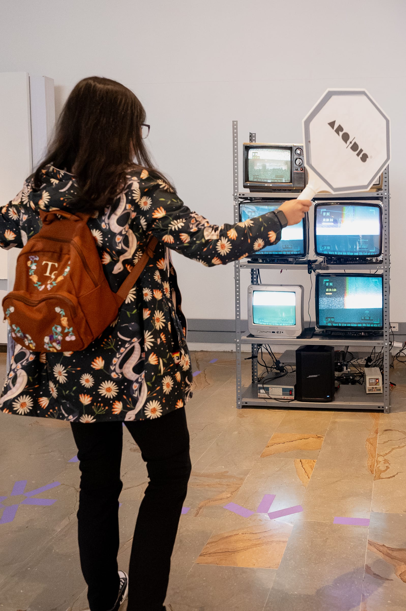 Vertical shot of a visitor holding an octagonal sign paddle in front of the 6-CRT totem on the gallery floor