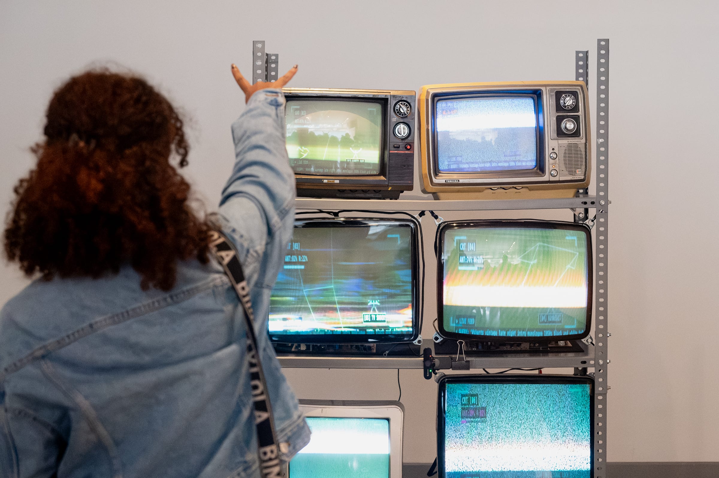 Gallery visitor raising an arm in front of the 6-CRT matrix to trigger pose recognition while green wireframe telemetry renders on screen